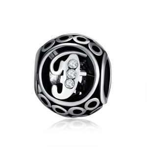Macro view of silver charm with hollow letter F design and sparkling cubic zirconia stones