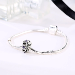 Silver snake chain bracelet with purple zircon floral charm on a white background