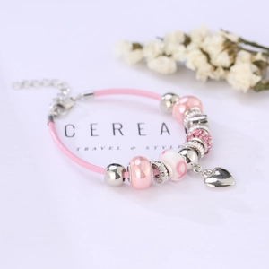 Close-up of pink ribbon cord bracelet with silver charms and a heart pendant