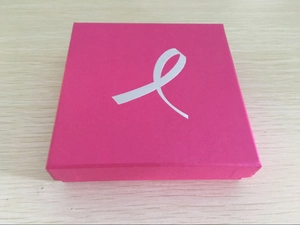 Close-up of a square pink gift box with a white ribbon logo on light wood background