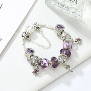 Detail of purple crystal beaded bracelet with S-letter heart and key charms on white leather