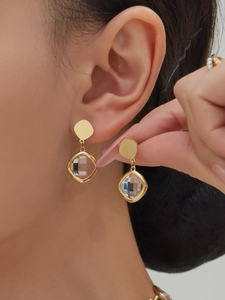 Detailed view of geometric gold drop earrings with faceted square crystal stones on a model