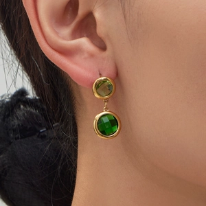 Vintage style gold earrings featuring two round faceted green gems worn on ear lobe