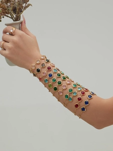 Close-up of stacked gold bracelets with colorful square faceted glass stones on a model