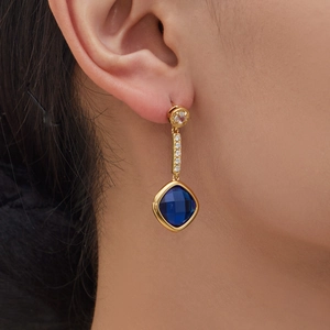 Golden drop earrings with blue square crystals and sparkling zircon details on model
