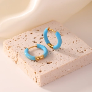 Detailed close-up of sky blue and gold hoop earrings on a luxury white silk background