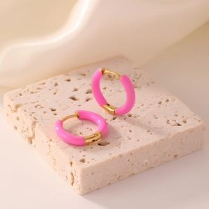 Macro detail of pink enamel hoop earrings on a textured stone stand with soft wavy fabric