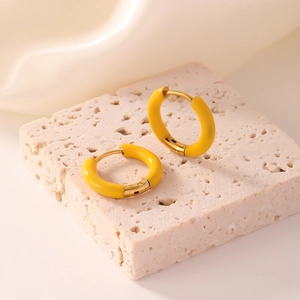 Macro detail of glossy yellow enamel gold hoop earrings on beige stone base