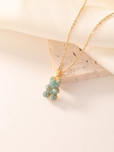 Detailed view of a golden bear pendant with blue turquoise pavé setting on soft silk fabric
