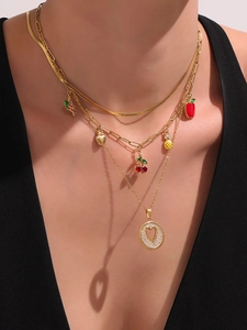 Detalle de collar multicapa dorado con dijes de frutas y colgante de corazón