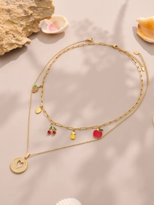 Detalle de collar doble dorado con dijes de frutas y colgante de corazón con circón