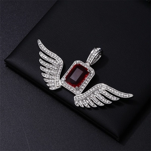 Macro view of iced out angel wing pendant with rectangle red gemstone and micro-pave diamonds
