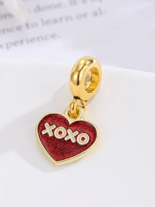 Makroaufnahme eines goldenen Herzanhängers mit rotem Glitzer-Emaille und XOXO-Schriftzug