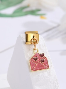 Vista macro de dije italiano dorado con sobre de purpurina rosa y corazones rojos