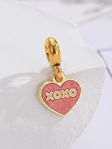 Makroaufnahme von pinkfarbenem XOXO-Herzanhänger mit Goldrand und Glitzer-Finish