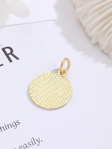Detailed macro view of a round gold pendant with striped relief texture and attachment ring