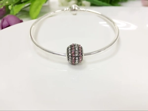 Detailed macro view of a silver bangle with a pink and white pavé crystal charm on a ceramic plate
