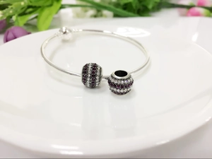 Detail of silver charm bracelet featuring two round purple and white crystal pave beads