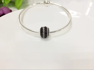 Macro shot of silver bead charm bracelet with purple and clear zircon stones in a ceramic dish