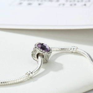 Vista macro dello charm con gemma viola e micro-pave su catena a serpente argentata