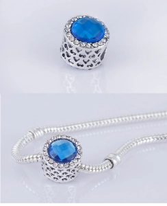 Dettaglio di un charm blu rotondo con zirconi bianchi e motivo a cuore traforato laterale