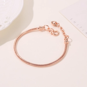 Detail van roségouden slangenarmband met hartvormige bedel en karabijnsluiting