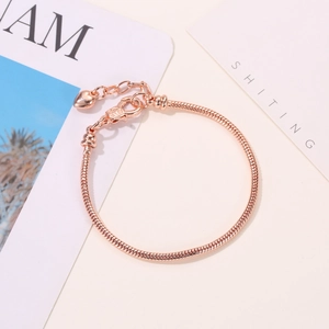 Detail van een roségouden slangenketting armband met karabijnsluiting en hart hanger
