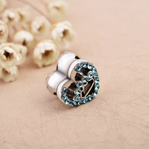 Macro detail of silver heart charm with light blue rhinestones on beige leather texture