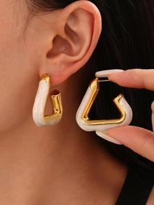 Detail of large gold-plated stainless steel triangle earrings with white enamel inlay