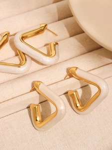 Detail of geometric V-shaped gold earrings with pearly white resin inlay on beige velvet