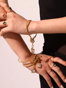 Macro shot of gold twist chain bracelets with zircon pendants and colorful gemstone rings