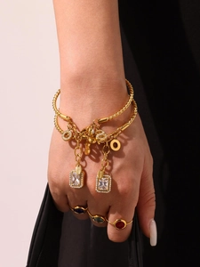 Close-up of gold layered bracelet with cubic zirconia charms and colorful gem rings