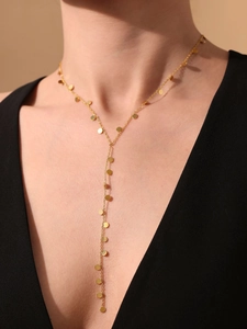 Detail of a gold Y-shaped tassel necklace with circular charms worn by a model in black