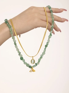 Detail of layered gold snake chain and green gemstone bead necklace with fishtail charm