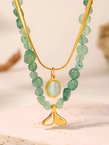 Detailed close-up of a double-layered necklace with green stones and a gold fishtail pendant