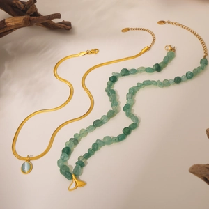 Detail of gold snake chain with blue gem and green stone necklace with fishtail pendant