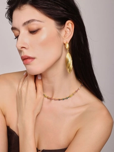Detail of large gold drop earrings with textured finish on model with gemstone necklace