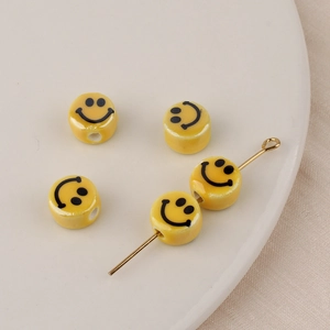 Detalle de cinco cuentas de cerámica amarillas con cara sonriente y aguja dorada para joyas