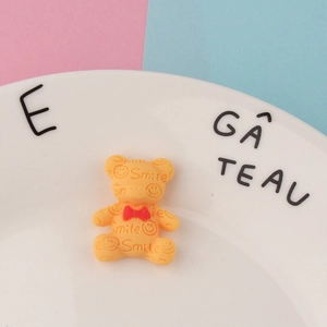 Makroaufnahme von gelbem Harzbär-DIY-Anhänger mit Smile-Gravur und roter Schleife