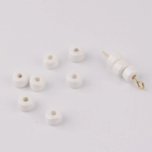 Macro shot of cream ceramic wheel beads with smooth glaze and gold needle for DIY jewelry