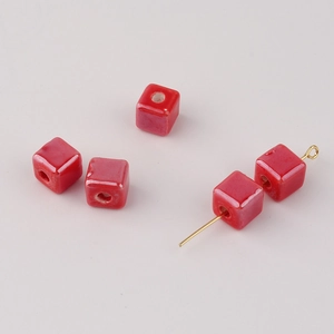 Macro detail of red glazed ceramic cube beads with golden pins for DIY jewelry making