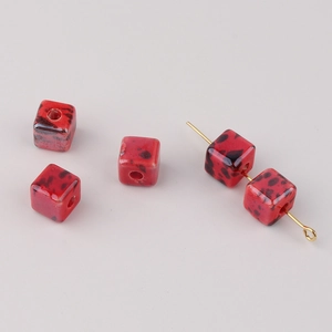 Detailed macro view of square red ceramic beads with black speckled pattern for DIY jewelry