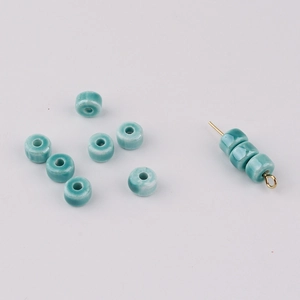 Close-up of light blue glazed ceramic beads on golden pins for DIY jewelry making