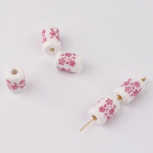 Macro shot of white cylindrical ceramic beads with delicate pink floral print for DIY jewelry