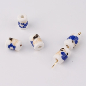 Macro detail of cylindrical white ceramic beads with blue floral patterns for DIY jewelry