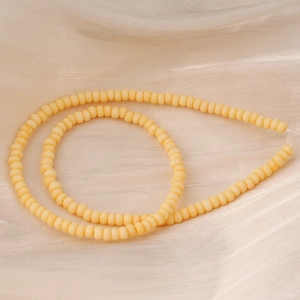 Gros plan de perles de verre jaune pâle mat sur soie beige pour bijoux artisanaux