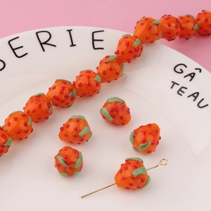 Detailed view of orange strawberry glass beads with green leaf accents for DIY jewelry
