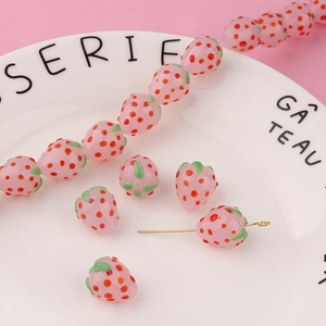 Detailed close-up of pink glass strawberry charms for handmade jewelry making