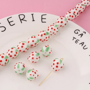 Macro view of handmade glass strawberry beads with gold eye pins on a pink background