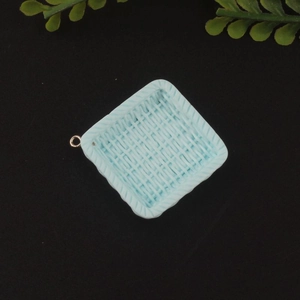 Macro detail of a light blue square resin woven basket charm with a gold loop for DIY jewelry